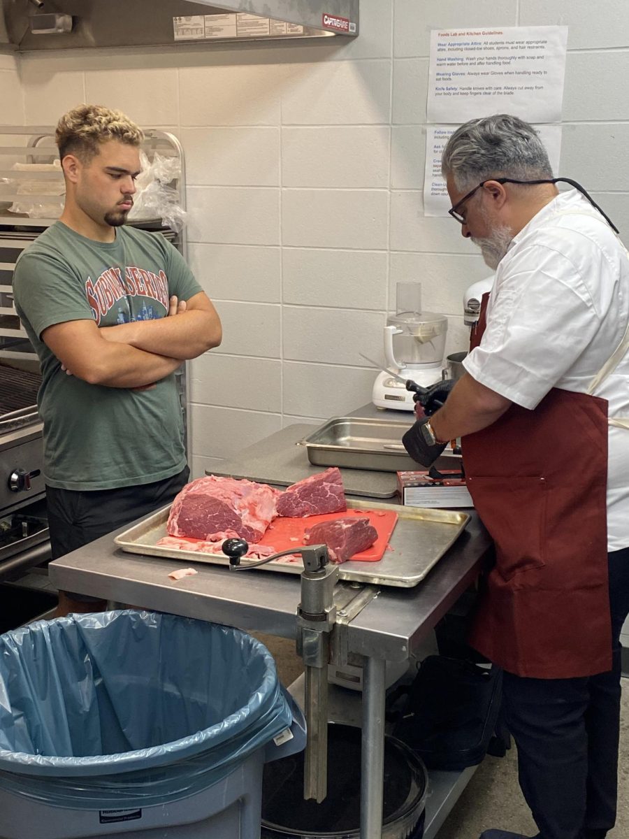 Senior Roman Hale (left) watches as Mr. Molina demonstrates how to prepare a roast on Wednesday, Aug. 28, in the classroom kitchen. The culinary class is responsible for feeding the football team before games.