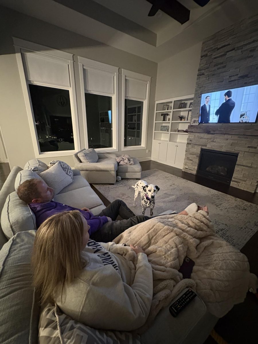 Jeff Travis (purple) and Heather Travis watching a Christmas movie. They watch the movie after it is dark outside.